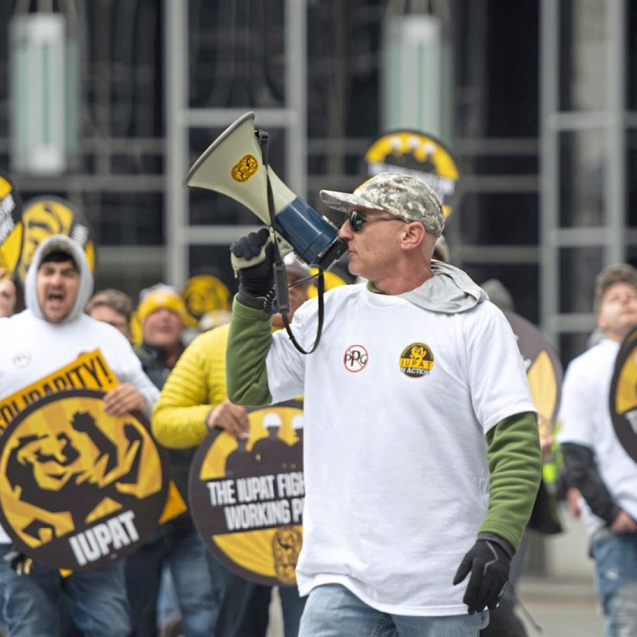 A photo of a man with a megaphone at a protest, signs with the words "solidarity" are seen.