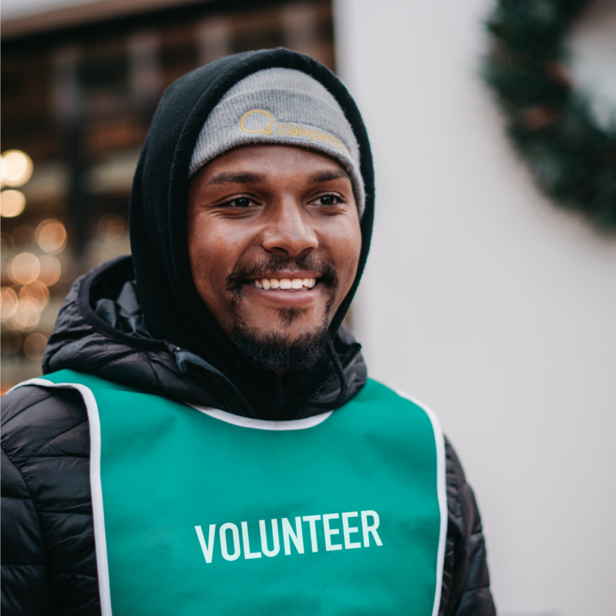 Photo of a person smiling and wearing a green volunteer vest.